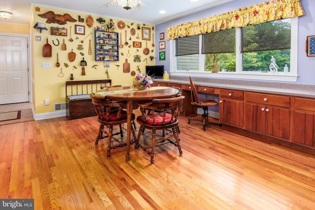 dining space with ornamental molding, light wood-type flooring, and built in desk