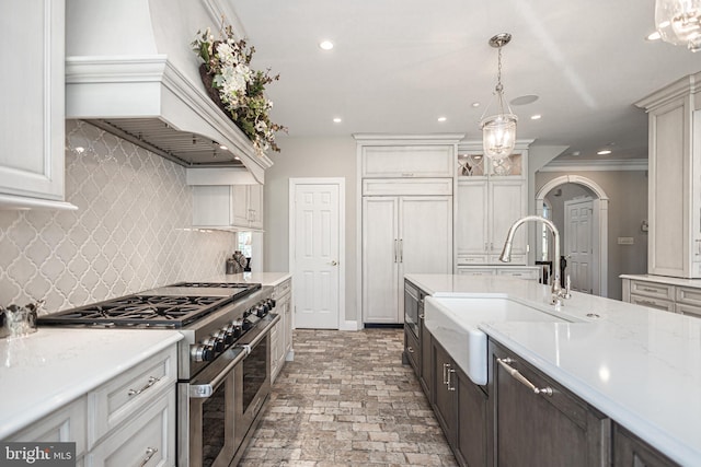 kitchen with dark brown cabinets, sink, custom exhaust hood, decorative backsplash, and range with two ovens