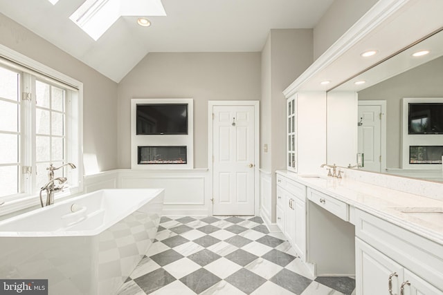 bathroom with vaulted ceiling with skylight, a tub, and vanity