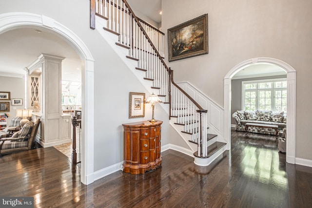 stairs with wood-type flooring, a towering ceiling, decorative columns, and crown molding