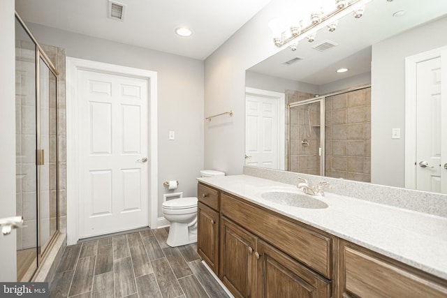 bathroom featuring a shower with door, toilet, and vanity