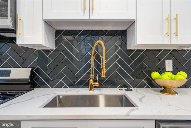 kitchen featuring tasteful backsplash, range, light stone countertops, sink, and white cabinets