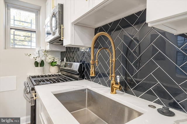 kitchen featuring stainless steel appliances, white cabinetry, backsplash, and light stone counters