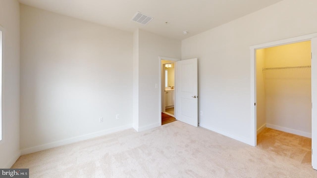 unfurnished bedroom featuring a spacious closet, light colored carpet, and a closet