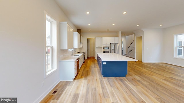 kitchen with sink, appliances with stainless steel finishes, white cabinetry, a center island, and light wood-type flooring