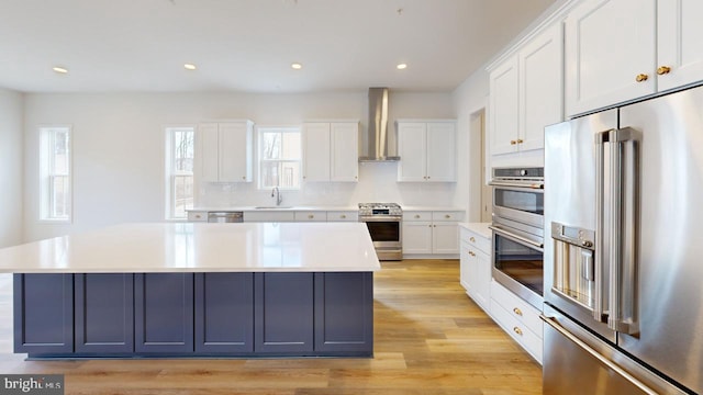 kitchen featuring white cabinetry, appliances with stainless steel finishes, a center island, and wall chimney range hood