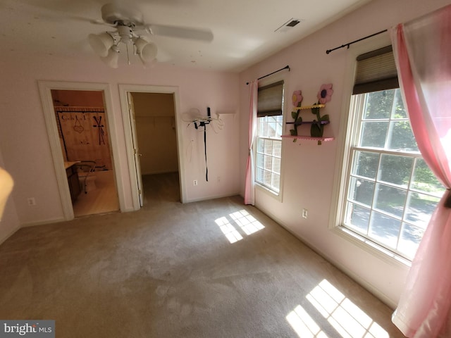 unfurnished bedroom featuring light carpet, a walk in closet, a closet, and ceiling fan