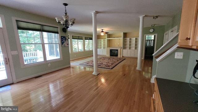 interior space featuring decorative columns, ceiling fan with notable chandelier, and light wood-type flooring