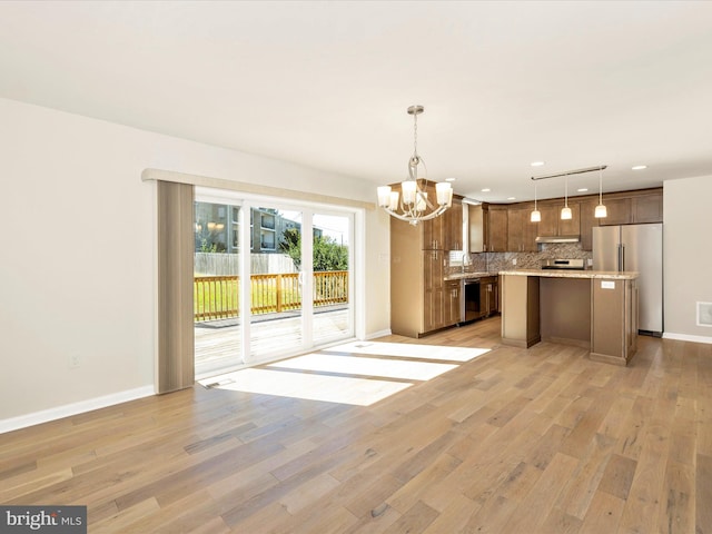 kitchen featuring hanging light fixtures, backsplash, stainless steel appliances, light hardwood / wood-style floors, and a center island