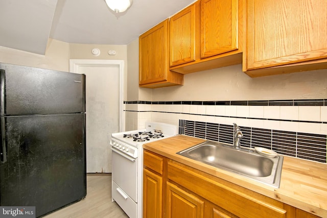 kitchen featuring gas range gas stove, butcher block counters, black refrigerator, light wood-type flooring, and sink