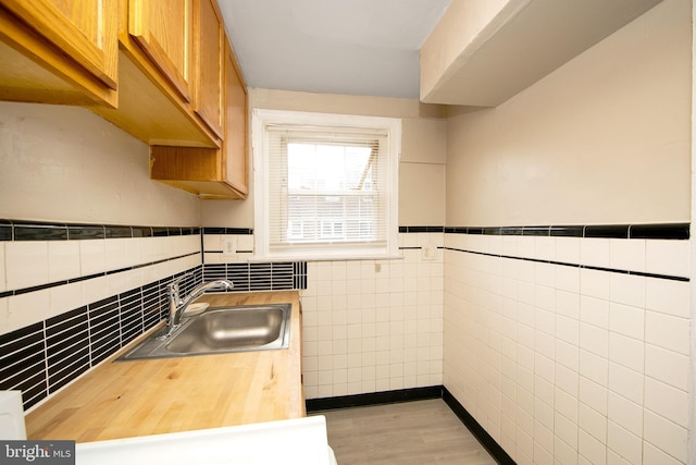 kitchen with tile walls, butcher block counters, a sink, light wood-type flooring, and wainscoting