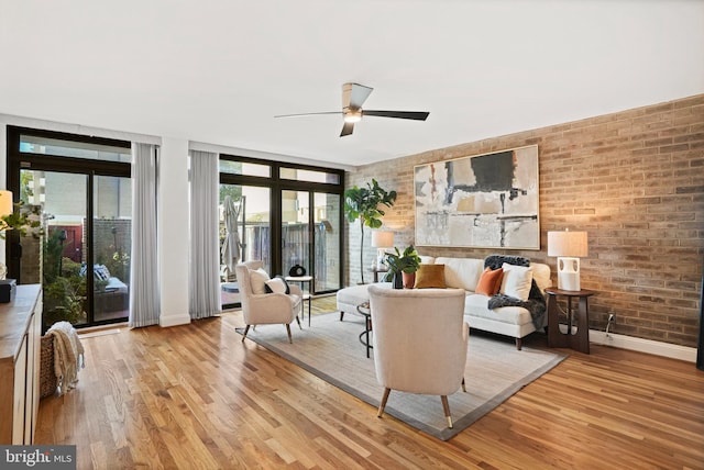 living room featuring floor to ceiling windows, light wood-type flooring, ceiling fan, and brick wall