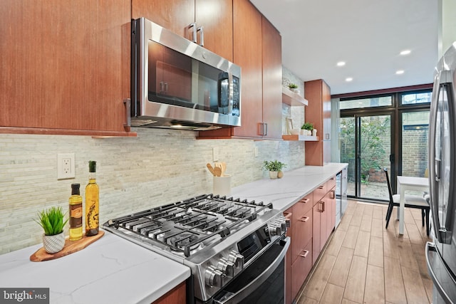 kitchen featuring light stone countertops, expansive windows, backsplash, light hardwood / wood-style floors, and appliances with stainless steel finishes