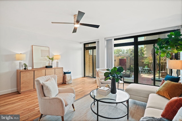 living room with ceiling fan, light hardwood / wood-style floors, and a wall of windows