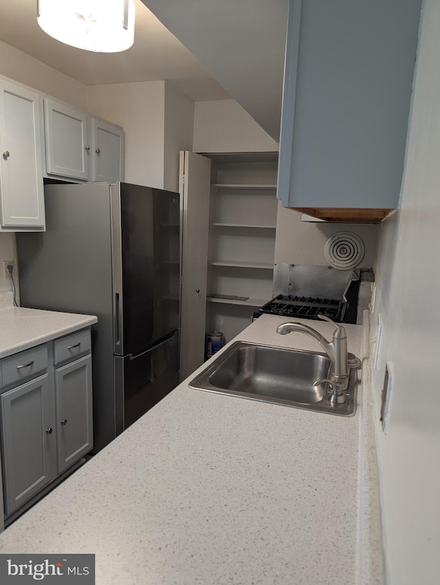 kitchen with gray cabinetry, sink, and stainless steel refrigerator