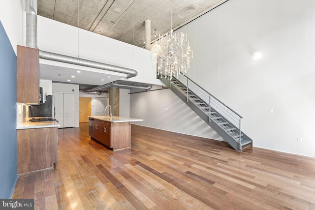 kitchen featuring an island with sink, sink, backsplash, a chandelier, and hardwood / wood-style floors