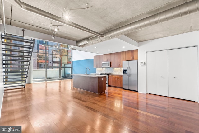 kitchen with appliances with stainless steel finishes, decorative backsplash, hardwood / wood-style flooring, a kitchen island with sink, and sink