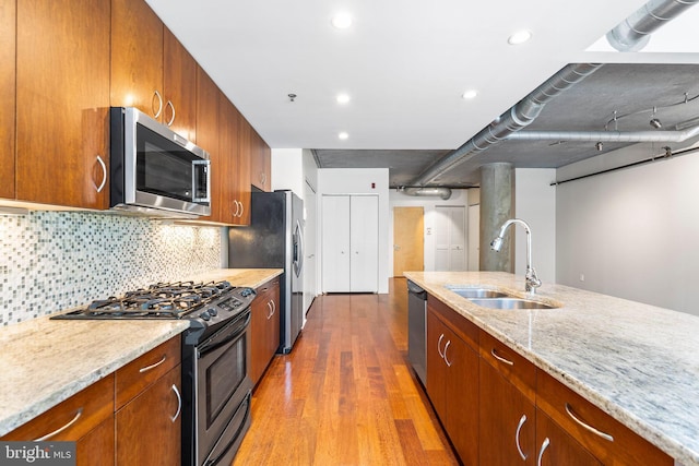 kitchen with light wood-type flooring, sink, tasteful backsplash, stainless steel appliances, and light stone countertops