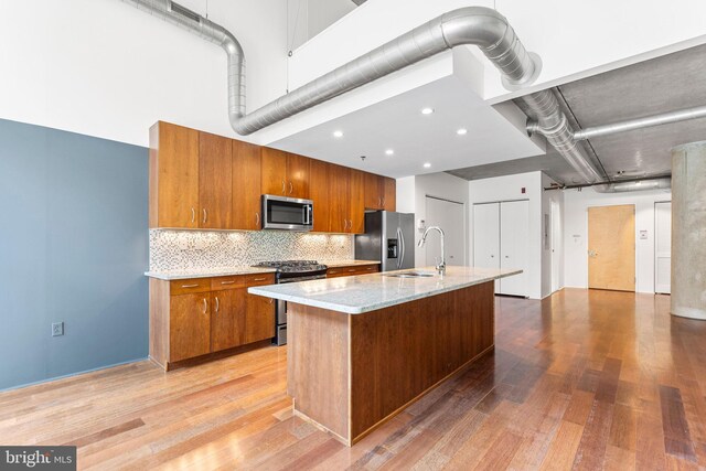 kitchen featuring sink, light hardwood / wood-style flooring, stainless steel appliances, decorative backsplash, and a center island with sink