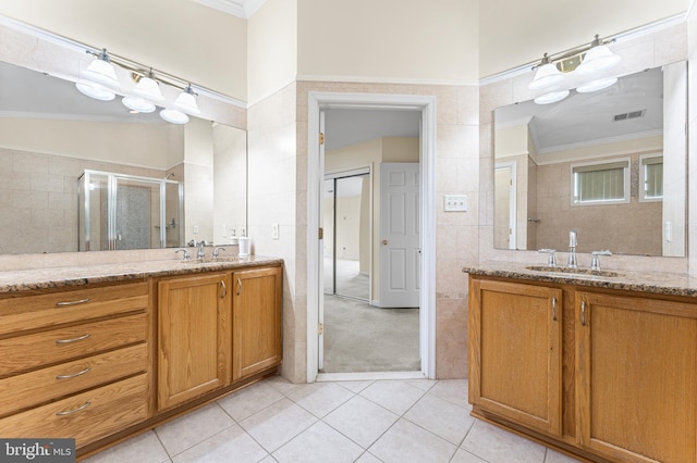 bathroom featuring vanity, ornamental molding, tile patterned floors, tile walls, and a shower with door