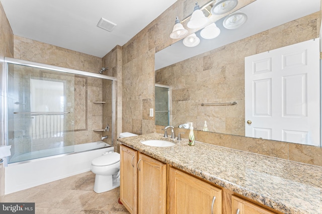 full bathroom with tile walls, vanity, tile patterned flooring, bath / shower combo with glass door, and toilet