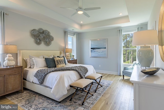 bedroom featuring ceiling fan, light hardwood / wood-style flooring, and a raised ceiling