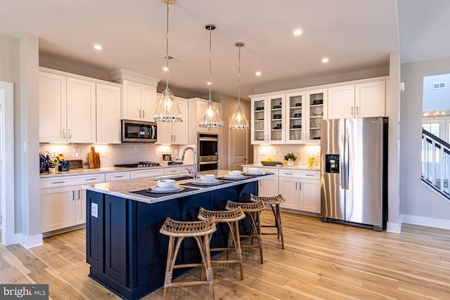 kitchen with appliances with stainless steel finishes, white cabinets, a kitchen island with sink, and decorative light fixtures