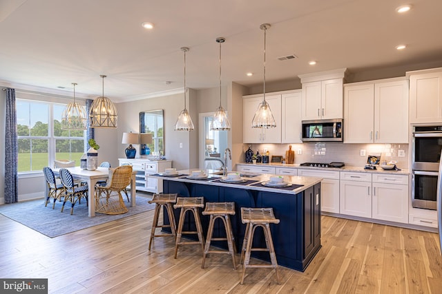 kitchen with a kitchen island with sink, appliances with stainless steel finishes, hanging light fixtures, and white cabinetry