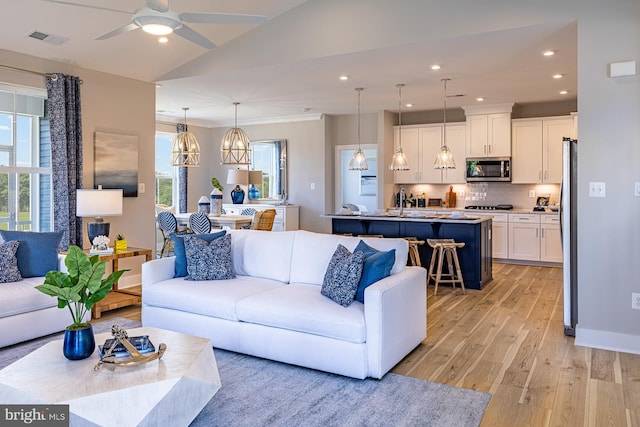 living room featuring ceiling fan with notable chandelier, light wood-type flooring, vaulted ceiling, and crown molding