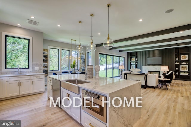 kitchen featuring appliances with stainless steel finishes, white cabinetry, light stone counters, pendant lighting, and a kitchen island with sink