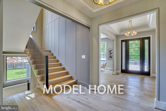 foyer entrance with ornamental molding, an inviting chandelier, light hardwood / wood-style flooring, and a tray ceiling