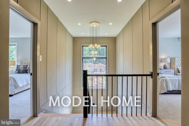 hallway with an inviting chandelier, a wealth of natural light, and light colored carpet