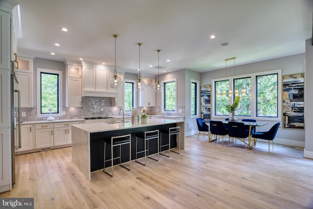 kitchen featuring an island with sink, white cabinets, decorative backsplash, light hardwood / wood-style flooring, and decorative light fixtures