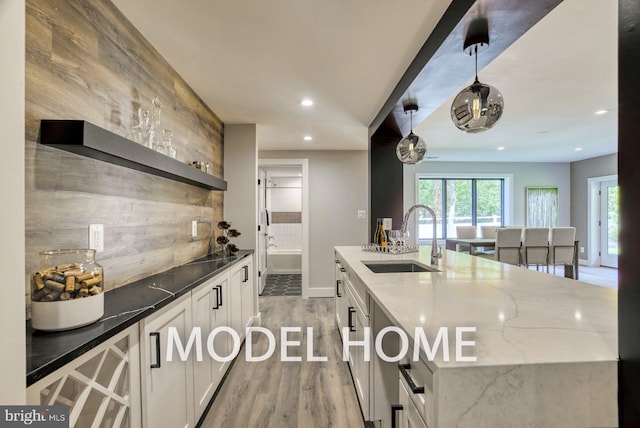 kitchen featuring light stone counters, a kitchen island with sink, sink, white cabinetry, and light hardwood / wood-style flooring