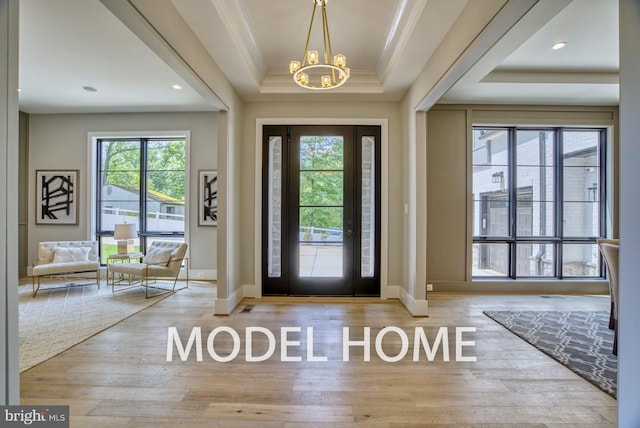 foyer with an inviting chandelier, a tray ceiling, hardwood / wood-style flooring, and crown molding