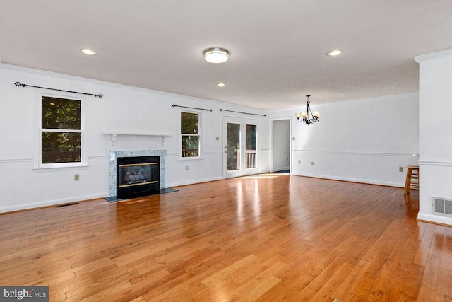 unfurnished living room with a healthy amount of sunlight, light hardwood / wood-style flooring, a premium fireplace, and a notable chandelier