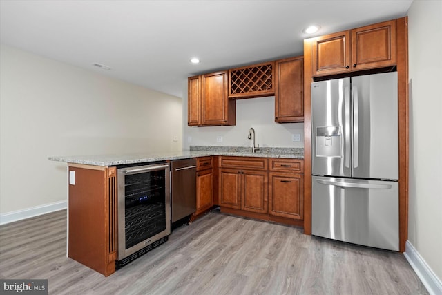 kitchen featuring appliances with stainless steel finishes, wine cooler, light stone counters, kitchen peninsula, and light wood-type flooring