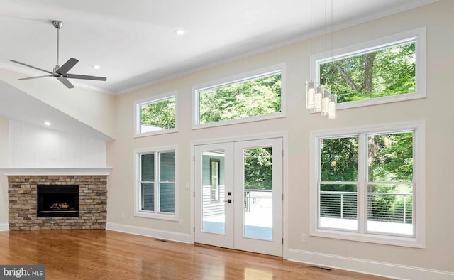 doorway to outside featuring a high ceiling, a fireplace, ornamental molding, french doors, and light wood-type flooring