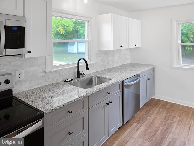 kitchen featuring sink, light hardwood / wood-style flooring, white cabinetry, stainless steel appliances, and light stone countertops