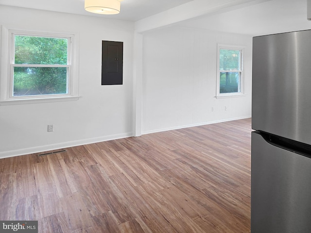 empty room with wood-type flooring, electric panel, beamed ceiling, and plenty of natural light