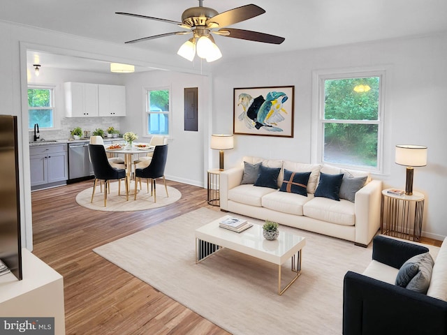 living room with light wood-type flooring, sink, ceiling fan, and electric panel