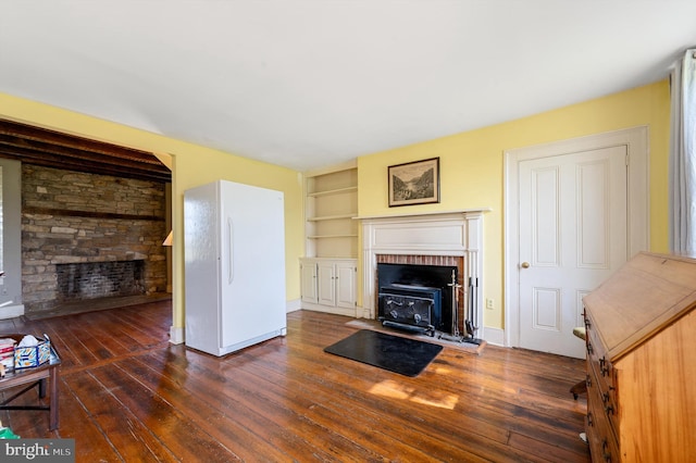 living room featuring dark wood-type flooring, a wood stove, and built in shelves