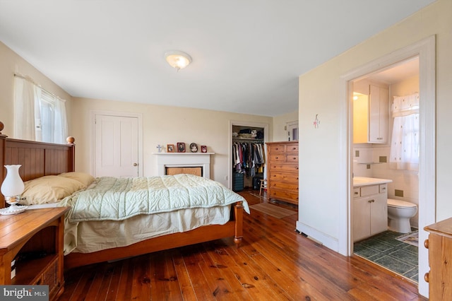 bedroom with tile walls, a walk in closet, ensuite bathroom, and dark hardwood / wood-style flooring