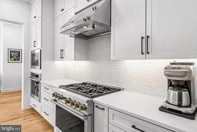 kitchen featuring stainless steel appliances, light wood-type flooring, decorative backsplash, and white cabinetry