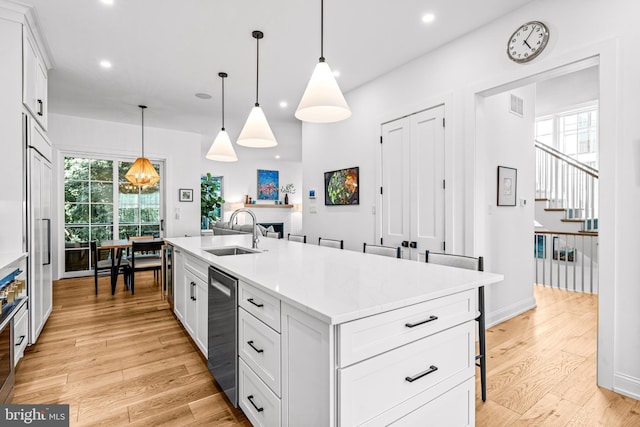 kitchen with an island with sink, white cabinets, pendant lighting, light hardwood / wood-style flooring, and sink