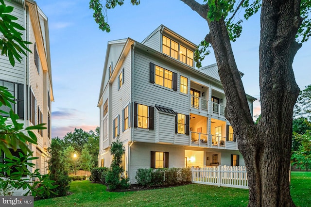 back house at dusk featuring a balcony and a yard