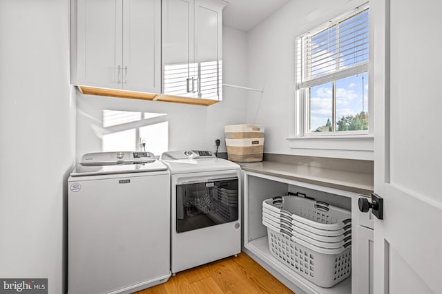 washroom featuring light wood-type flooring, washer and clothes dryer, and cabinets