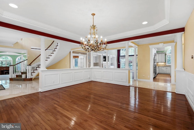 unfurnished dining area with decorative columns, a chandelier, hardwood / wood-style floors, and ornamental molding