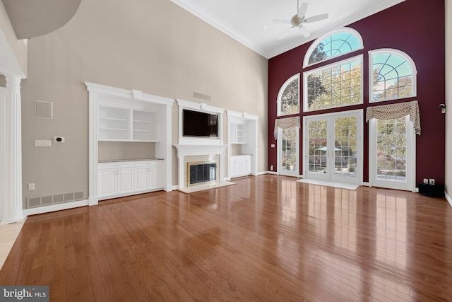 unfurnished living room featuring crown molding, a towering ceiling, ornate columns, hardwood / wood-style flooring, and ceiling fan