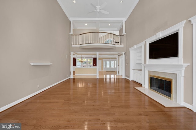 unfurnished living room featuring hardwood / wood-style floors, a towering ceiling, ceiling fan with notable chandelier, and crown molding